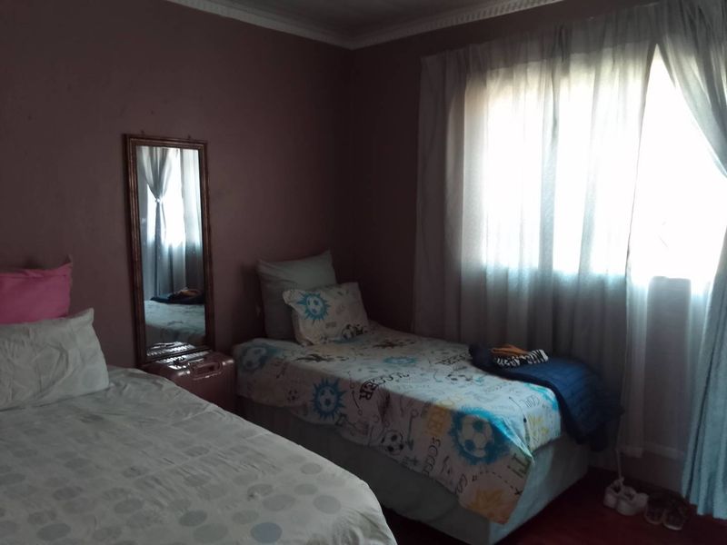 A bedroom featuring crown molding and a window with curtains, currently showing signs of wear on the wall surfaces.