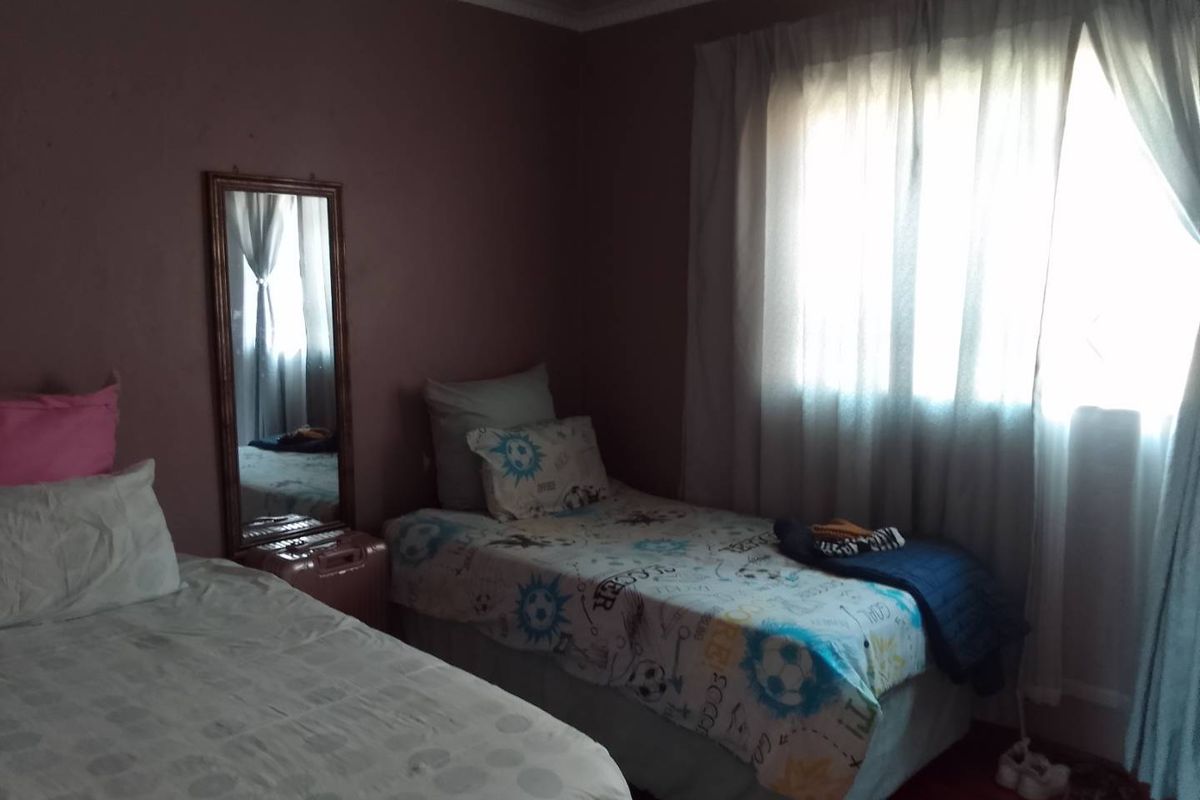 A bedroom featuring crown molding and a window with curtains, currently showing signs of wear on the wall surfaces.