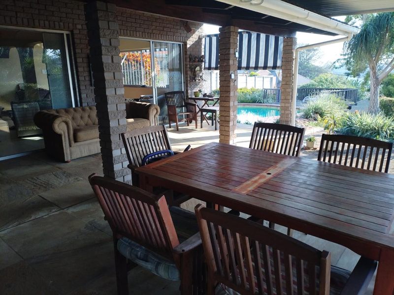 Covered outdoor patio area featuring brick pillars, paved flooring, and direct access to the swimming pool and garden.