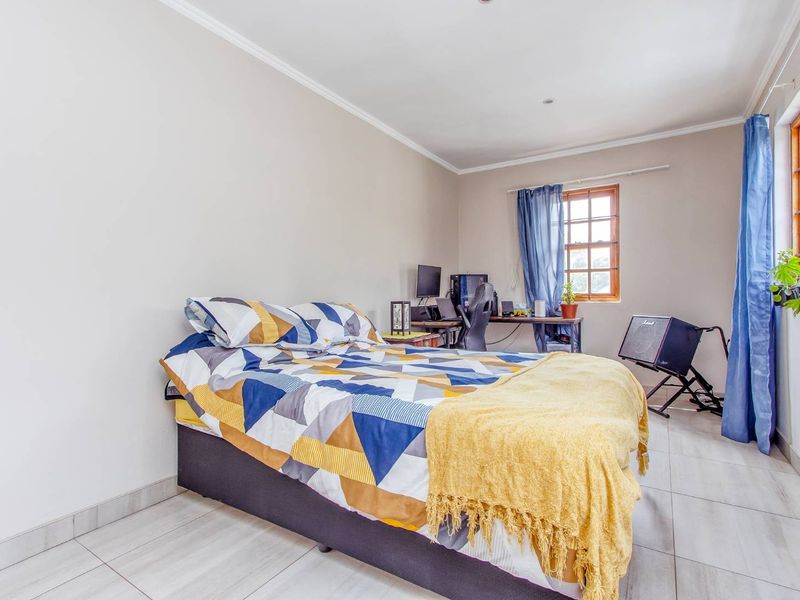 A functional bedroom featuring tiled flooring, timber-framed windows, and neutral wall finishes, offering a versatile space for rest or study.