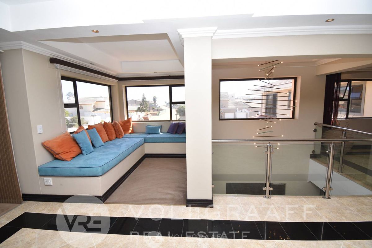 A bright living area featuring a built-in window seat, tiled flooring with decorative inlay, and a modern glass balustrade overlooking the lower level.