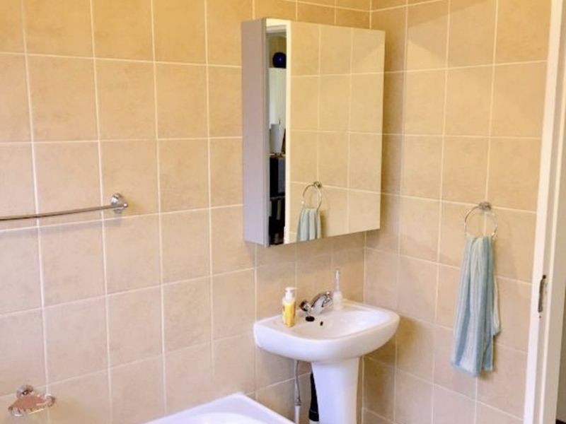 A functional bathroom featuring a pedestal basin, built-in bathtub, and full-height wall tiling with a mirrored medicine cabinet.