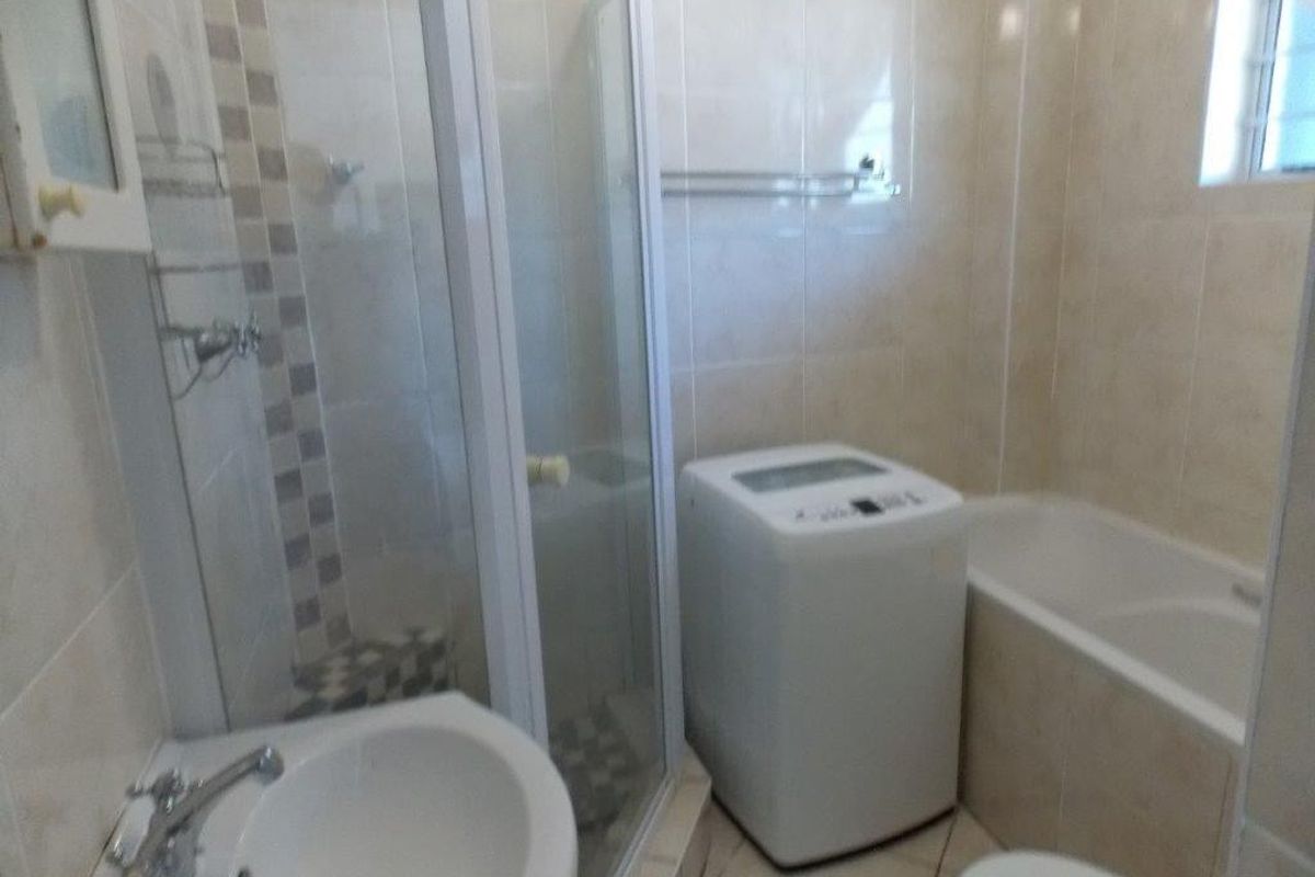 A functional bathroom featuring a shower enclosure, bathtub, and pedestal basin with neutral wall and floor tiling.