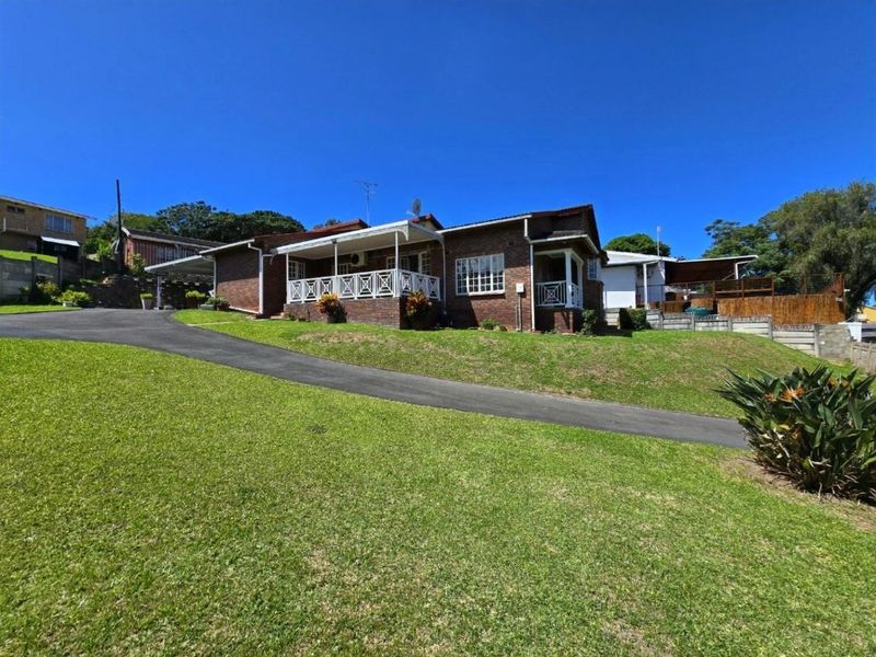 A well-maintained brick house featuring a covered front patio, an asphalt driveway, and a spacious lawn area.