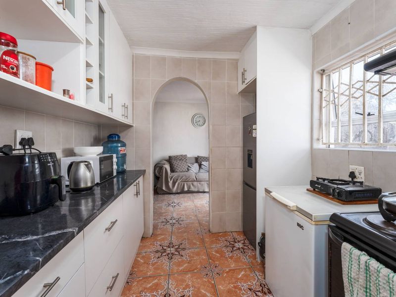 A functional kitchen featuring built-in cabinetry, stone countertops, and tiled finishes, leading through an archway into the adjacent living area.