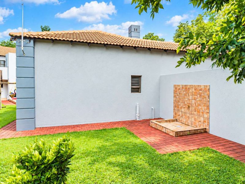 Rear exterior view of the property featuring a paved area, lawn, and a built-in outdoor shower facility.