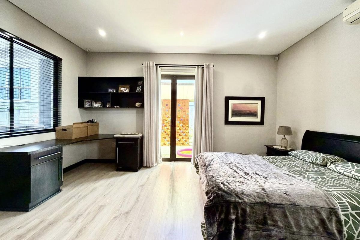 Spacious bedroom featuring light wood-look flooring, built-in desk and shelving unit, recessed lighting, and glass sliding doors providing access to the outdoor area.