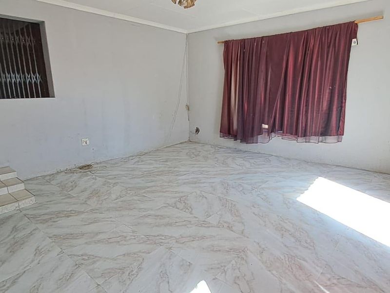 An empty living room featuring tiled flooring, a stepped transition to an adjacent area, and a security gate.