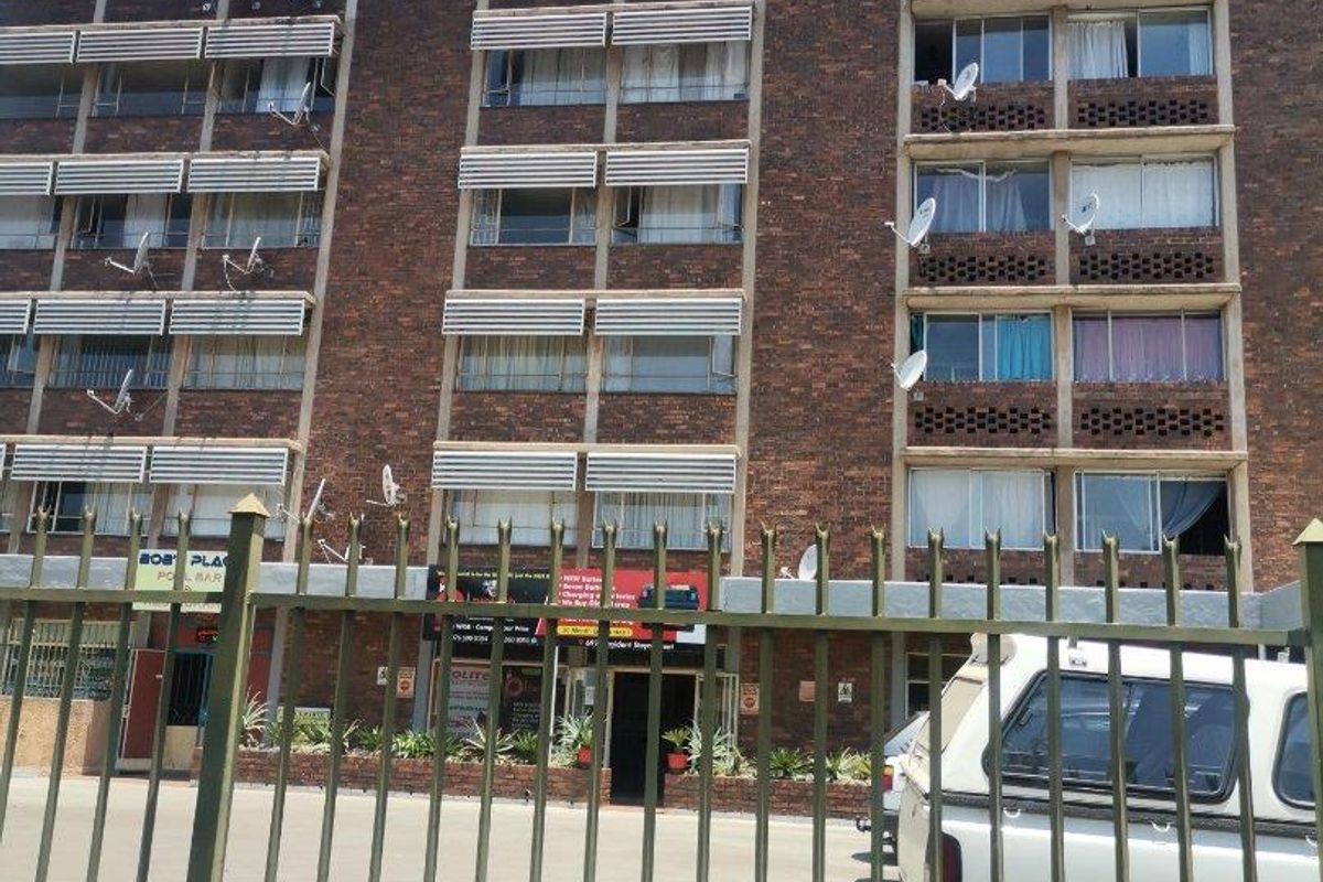 Front elevation of a multi-story brick retail and residential building featuring metal security fencing and multiple satellite dish installations.