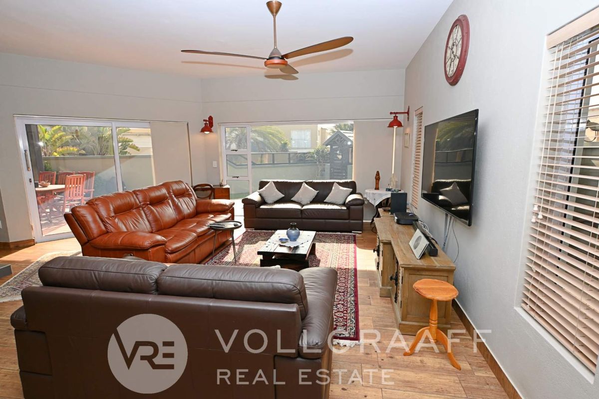 Spacious living room featuring wood-look tile flooring, a ceiling fan, and large sliding glass doors providing access to the outdoor patio area.