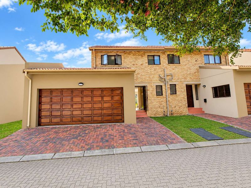 Front elevation of a townhouse featuring a brick facade, paved driveway, and a double garage with wooden doors.