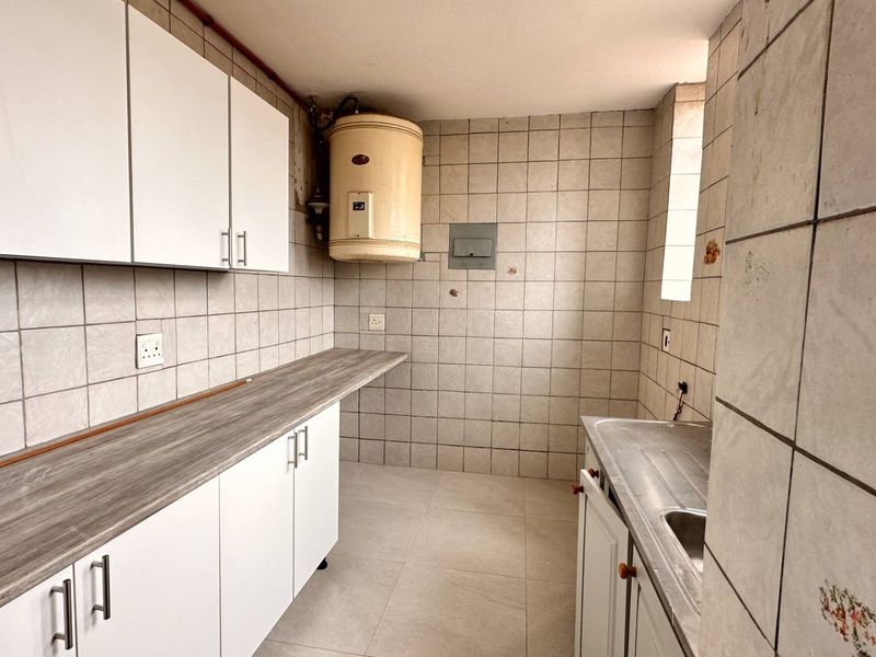 A functional kitchen space featuring white cabinetry, laminate countertops, a stainless steel sink, and tiled finishes throughout, ready for modernization.