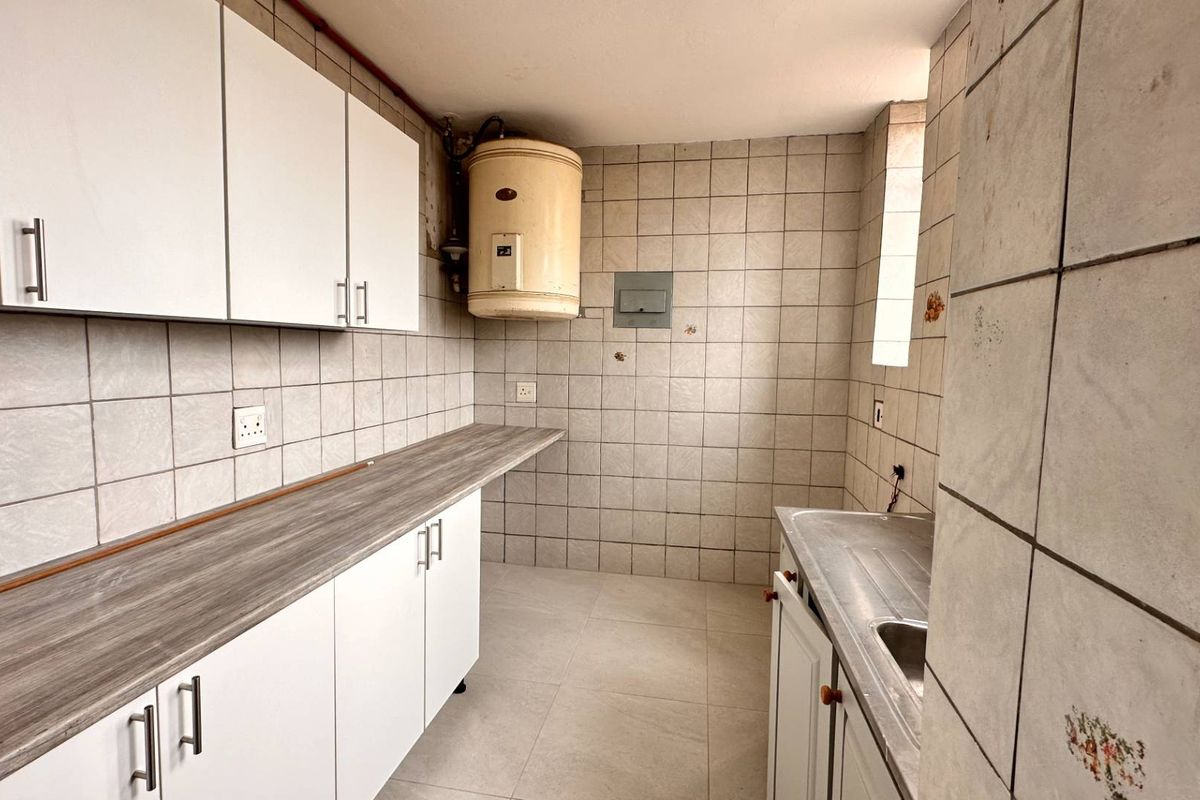 A functional kitchen space featuring white cabinetry, laminate countertops, a stainless steel sink, and tiled finishes throughout, ready for modernization.