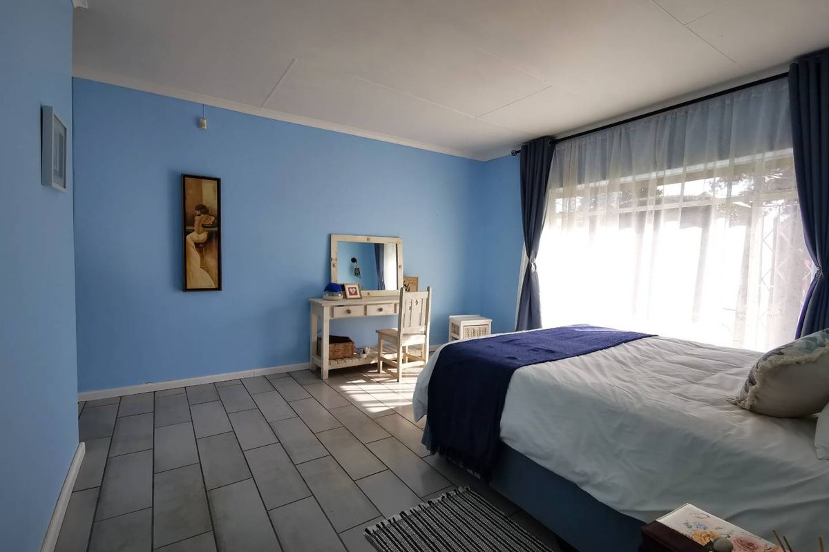 A spacious bedroom featuring light blue walls, tiled flooring, and a large window allowing for ample natural light.
