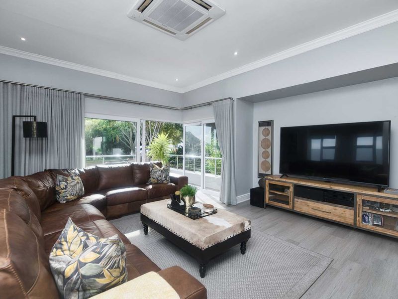 A well-maintained living room featuring laminate flooring, recessed lighting, ducted air conditioning, and large sliding glass doors providing natural light and outdoor access.