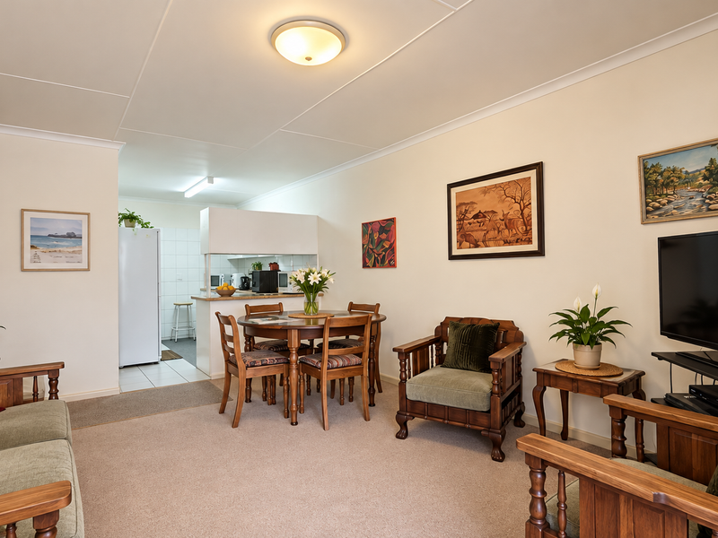Open plan living and dining area featuring neutral walls, carpeted flooring, and a functional kitchen pass-through with a breakfast bar.