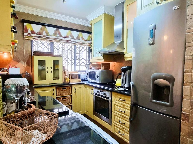 A functional kitchen featuring yellow cabinetry, black granite countertops, stainless steel appliances, and a tiled backsplash with a window security gate.