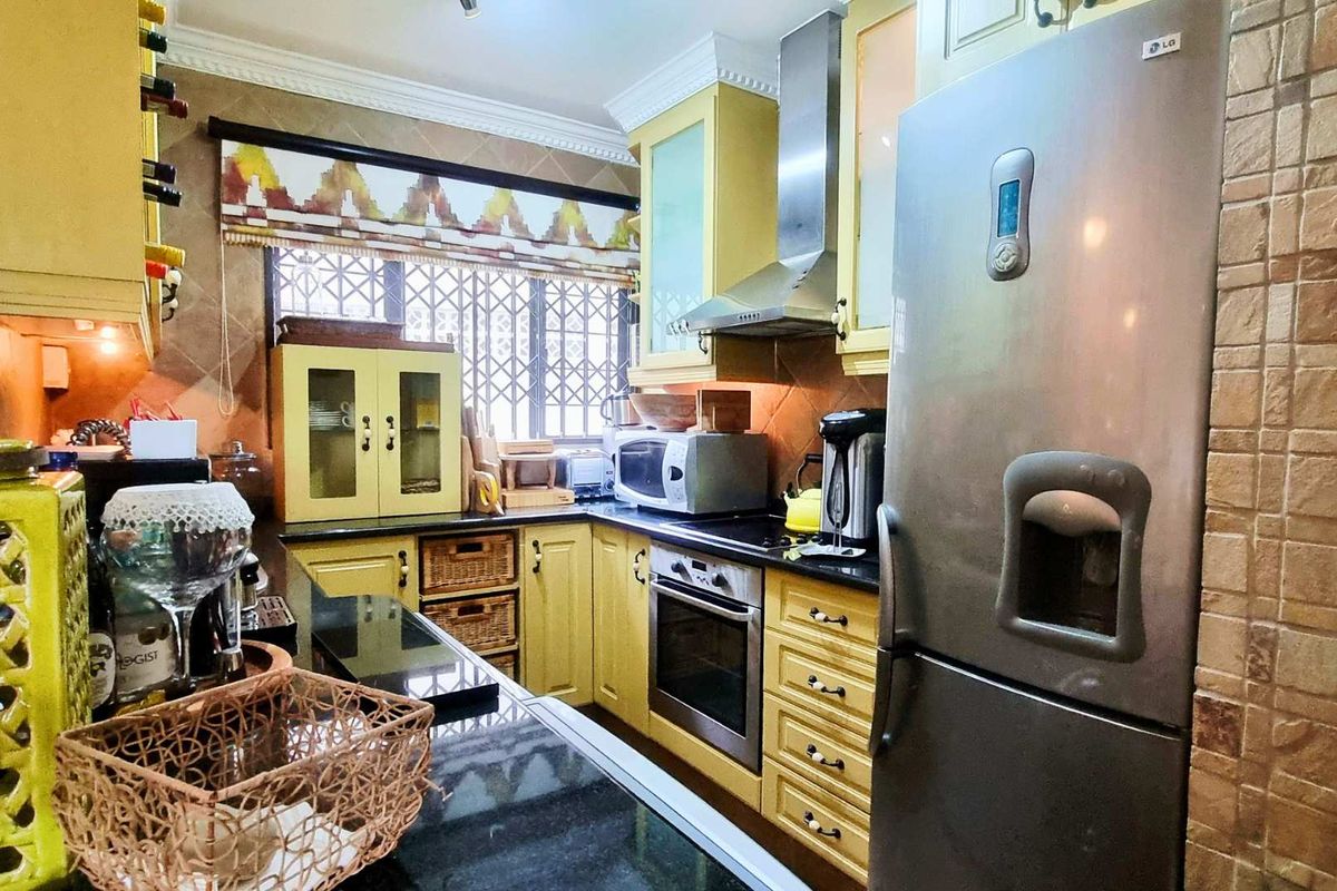A functional kitchen featuring yellow cabinetry, black granite countertops, stainless steel appliances, and a tiled backsplash with a window security gate.