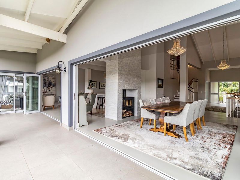 Spacious open-plan living and dining area featuring a stone-clad fireplace, vaulted ceilings, and seamless flow to a covered patio through large sliding doors.