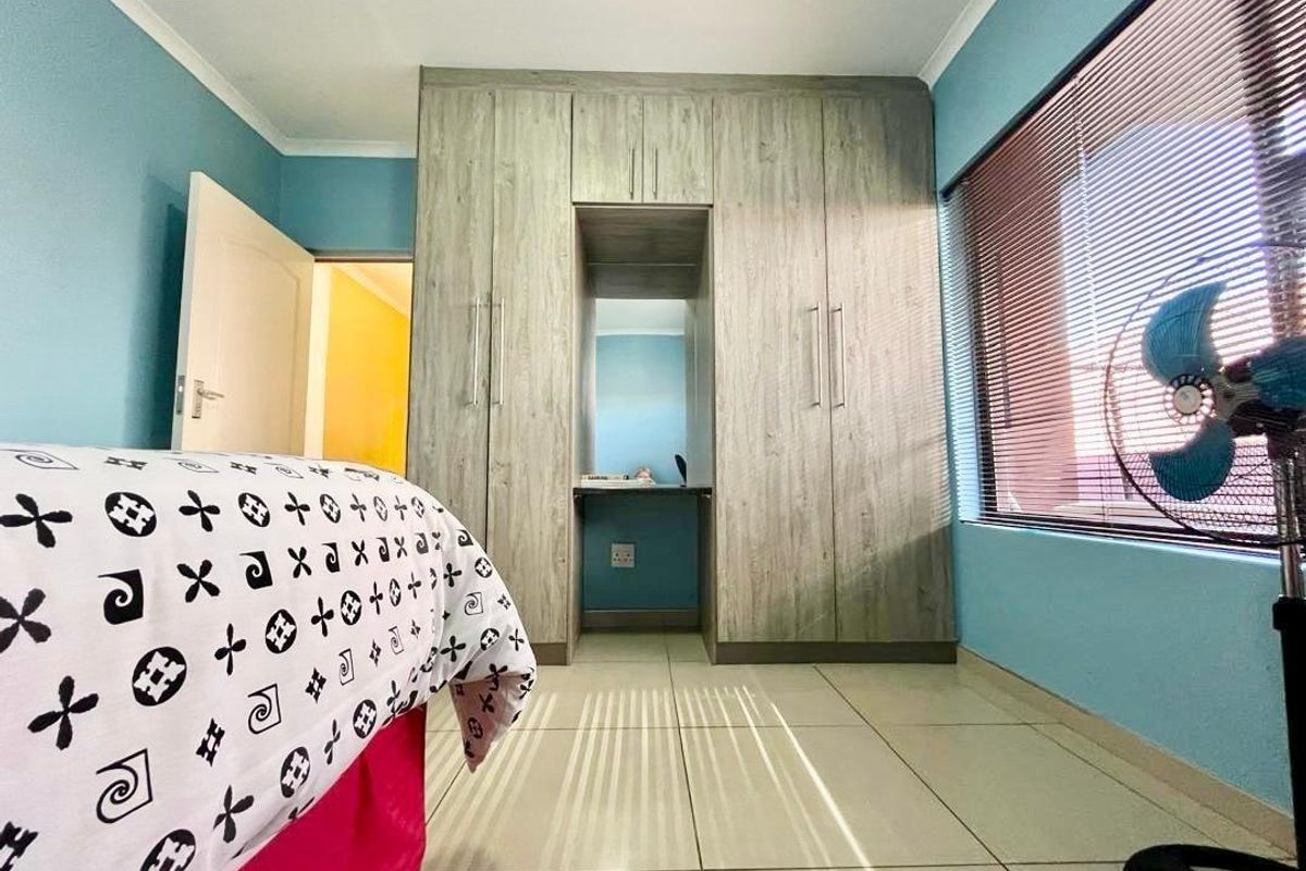 A bedroom featuring built-in wooden cabinetry with an integrated vanity area, tiled flooring, and horizontal window blinds.
