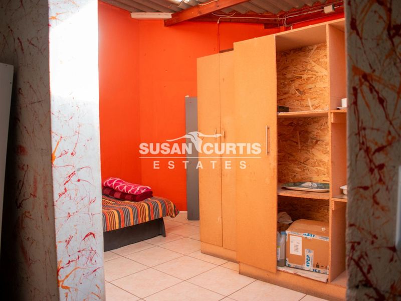 A bedroom featuring tiled flooring, exposed timber rafters, and a built-in wardrobe, requiring cosmetic updates to improve the overall aesthetic.