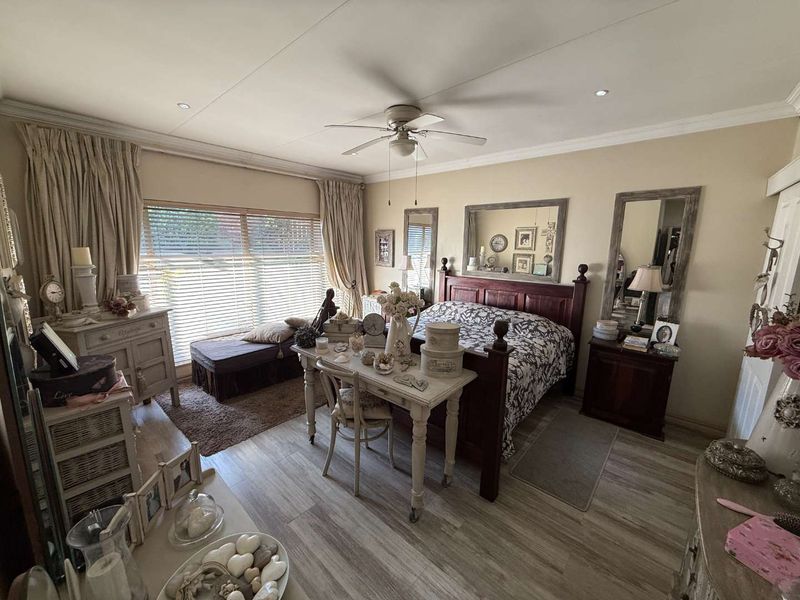 A well-maintained bedroom featuring wood-look tile flooring, a ceiling fan, and large windows with venetian blinds, offering a comfortable and functional living space.