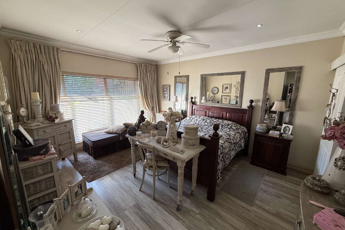 A well-maintained bedroom featuring wood-look tile flooring, a ceiling fan, and large windows with venetian blinds, offering a comfortable and functional living space.