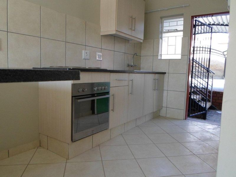 A functional kitchen featuring light-toned built-in cabinetry, tiled backsplash, integrated oven and hob, and direct access to an exterior area via a security gate.