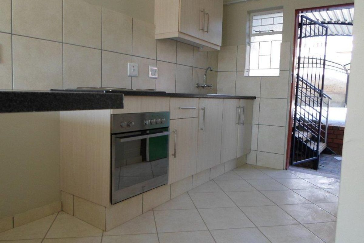 A functional kitchen featuring light-toned built-in cabinetry, tiled backsplash, integrated oven and hob, and direct access to an exterior area via a security gate.