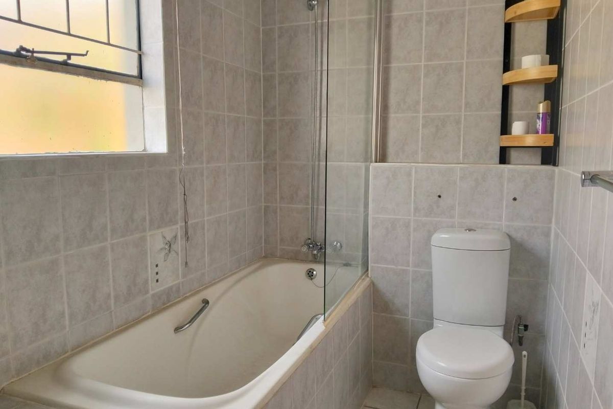 A functional bathroom featuring a bathtub with a glass shower screen, a toilet, and neutral wall tiling. Requires minor cosmetic repairs to wall finishes.