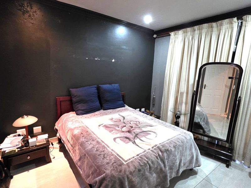 A bedroom featuring dark painted walls with crown molding, tiled flooring, and floor-to-ceiling curtains.