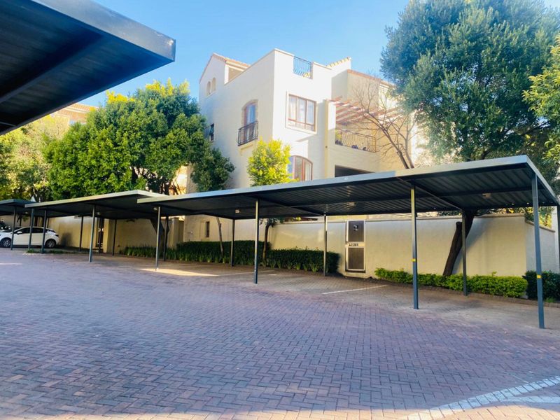 Exterior view of the apartment complex featuring covered parking bays, paved driveway, and well-maintained landscaping.