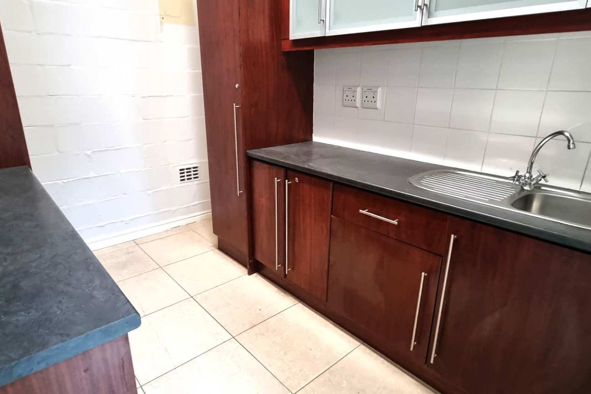 A functional kitchenette area featuring dark wood cabinetry, a stainless steel sink, and tiled splashbacks, suitable for office staff use.