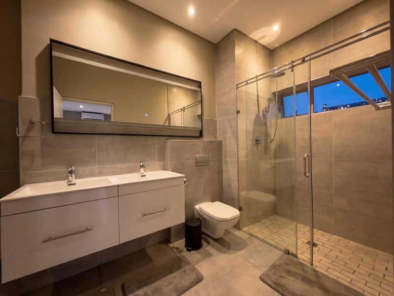Modern bathroom featuring a double vanity, wall-mounted toilet, and a spacious glass-enclosed shower with contemporary tiling and recessed lighting.