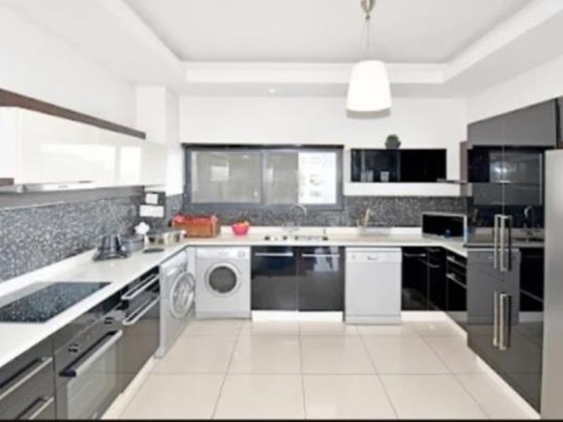 Modern kitchen featuring high-gloss cabinetry, stone countertops, integrated appliances, tiled backsplash, and sleek pendant lighting in a clean, contemporary layout.
