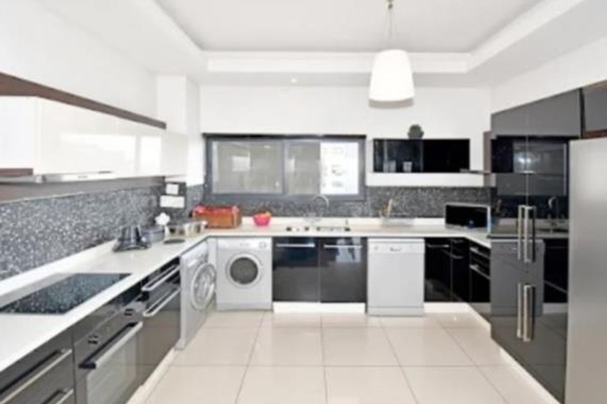 Modern kitchen featuring high-gloss cabinetry, stone countertops, integrated appliances, tiled backsplash, and sleek pendant lighting in a clean, contemporary layout.