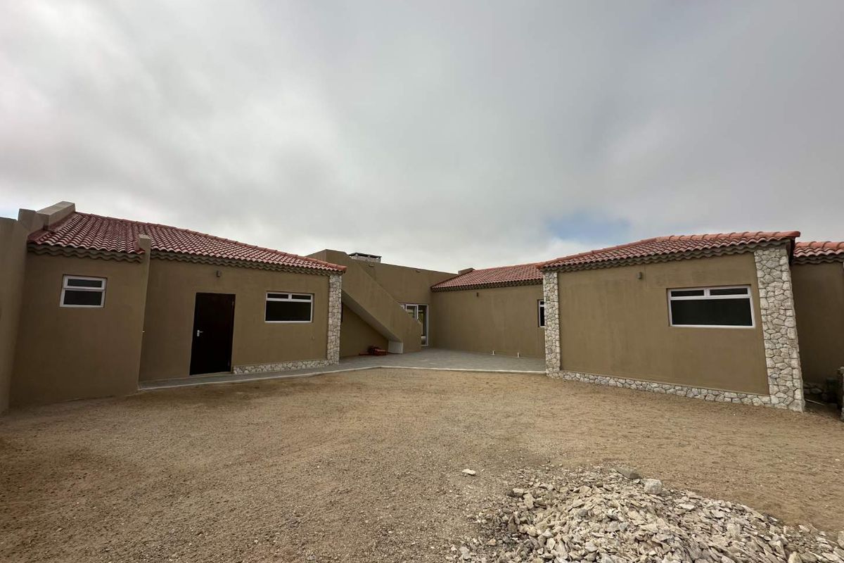 Rear view of the property featuring a paved courtyard, terracotta tiled roof, and stone-accented exterior walls with an external staircase.