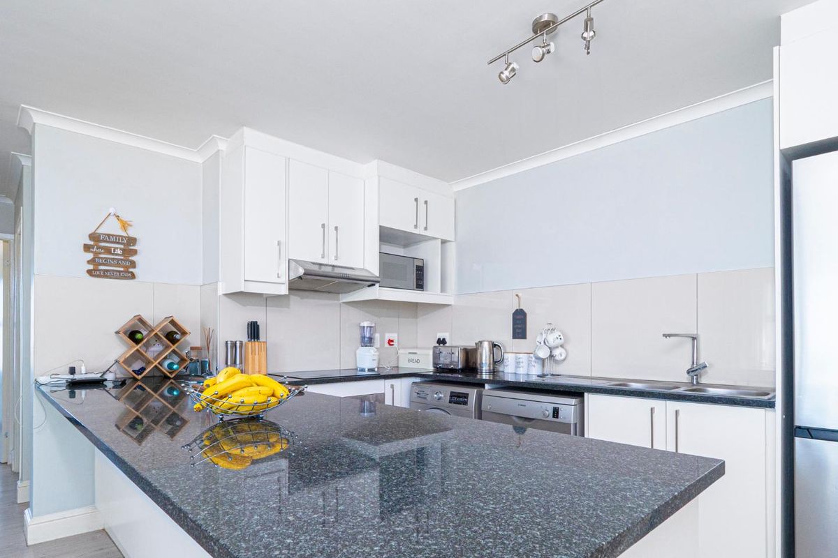 Modern kitchen featuring dark granite countertops, white cabinetry, tiled backsplash, and integrated appliance spaces, offering a clean and functional culinary area.