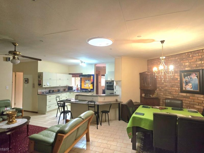Spacious open-plan living and dining area featuring an exposed brick feature wall, tiled flooring, and a functional kitchen with a breakfast bar.