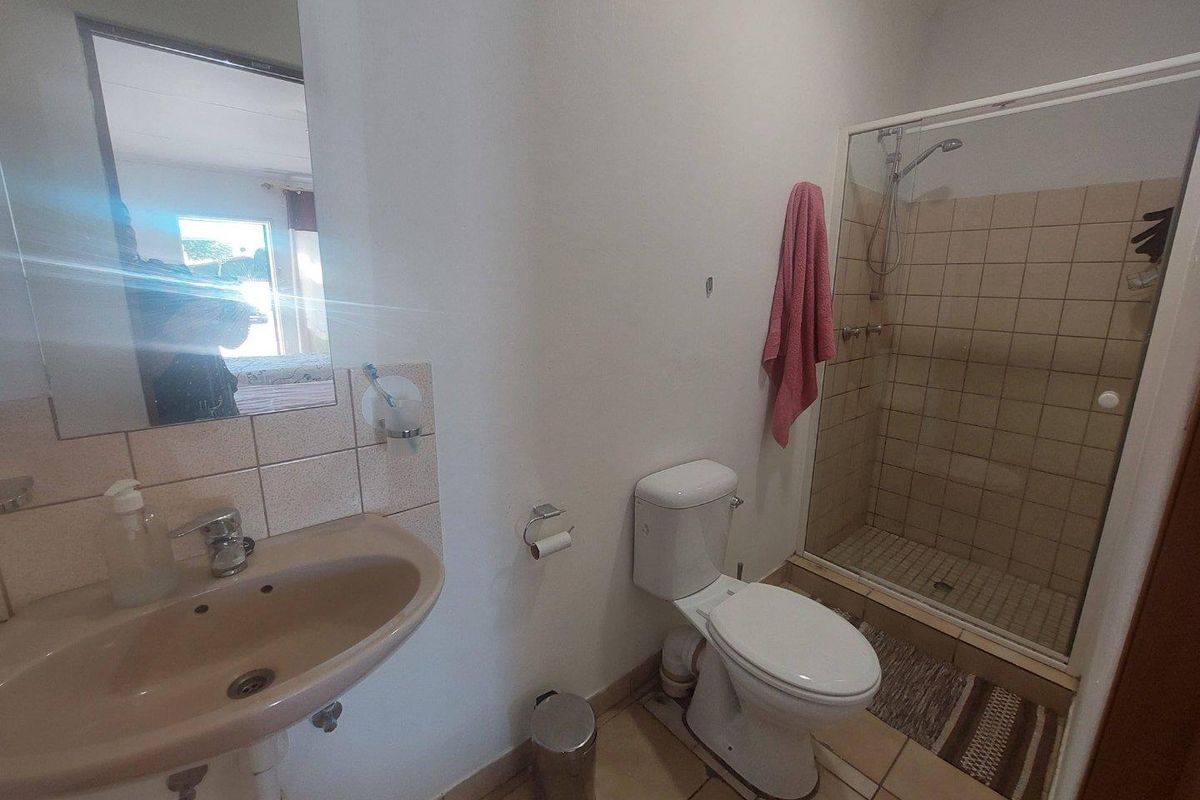 A functional bathroom featuring a shower enclosure with tiled walls, a pedestal basin, and a standard toilet.