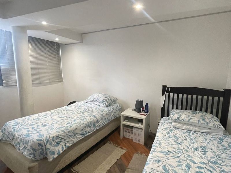 A bedroom featuring laminate flooring, recessed downlighting, and venetian blinds, providing a functional space with a structural column.