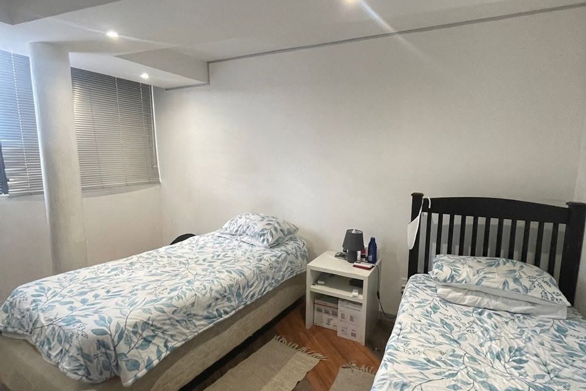 A bedroom featuring laminate flooring, recessed downlighting, and venetian blinds, providing a functional space with a structural column.