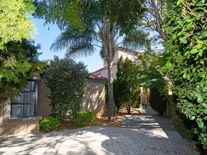 A well-maintained front exterior view featuring a paved driveway, mature landscaping, and a stucco facade with tiled roof detailing.