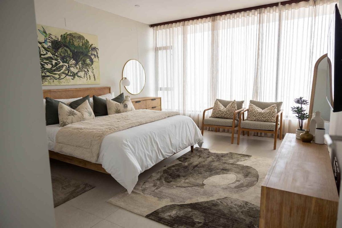 A spacious, well-lit bedroom featuring large floor-to-ceiling windows with sheer curtains and neutral tiled flooring.
