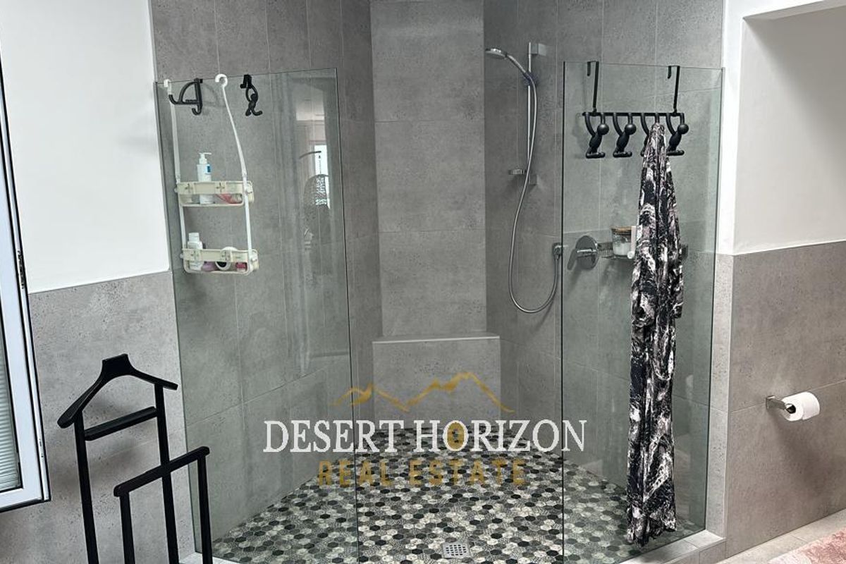 Modern bathroom featuring a walk-in shower with glass enclosure, grey wall tiling, and a decorative mosaic floor tile finish.