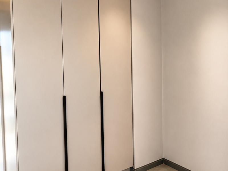 A clean, modern bedroom space featuring neutral-toned built-in wardrobes, recessed ceiling lighting, and contemporary tiled flooring.