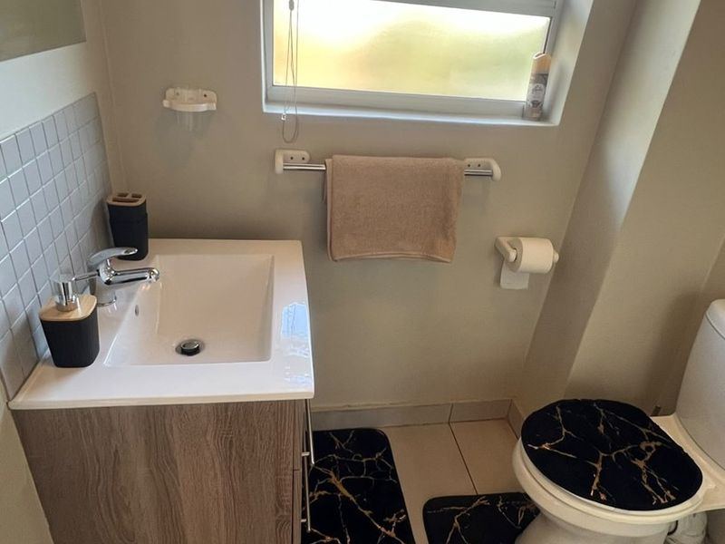 A compact, well-maintained bathroom featuring a modern vanity cabinet with a ceramic basin, tiled flooring, and a functional toilet.