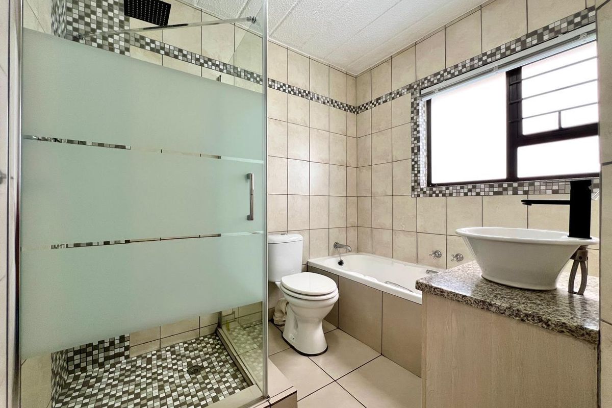 A functional bathroom featuring a glass-enclosed shower, a separate bathtub, a vanity with a vessel sink, and tiled walls.