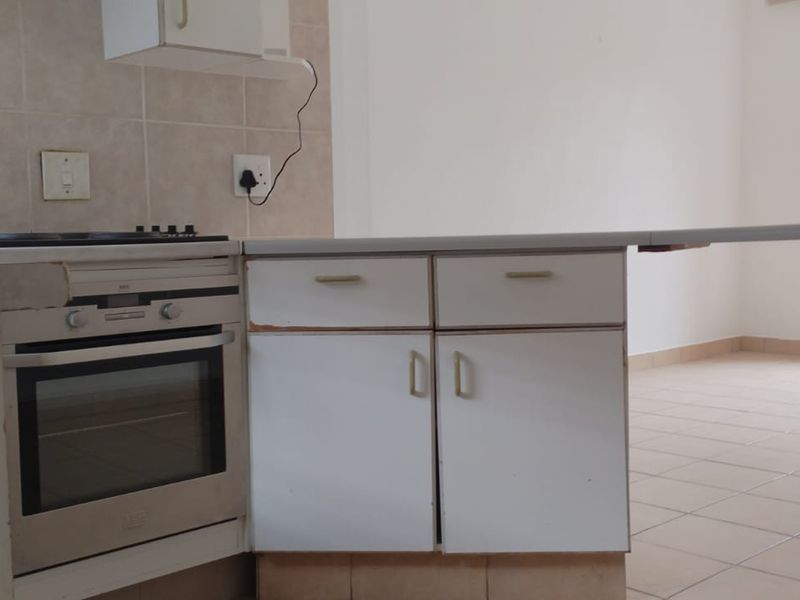 Open plan kitchen and living area featuring tiled floors, built-in oven and hob, and a breakfast counter, presenting a blank canvas for renovation.