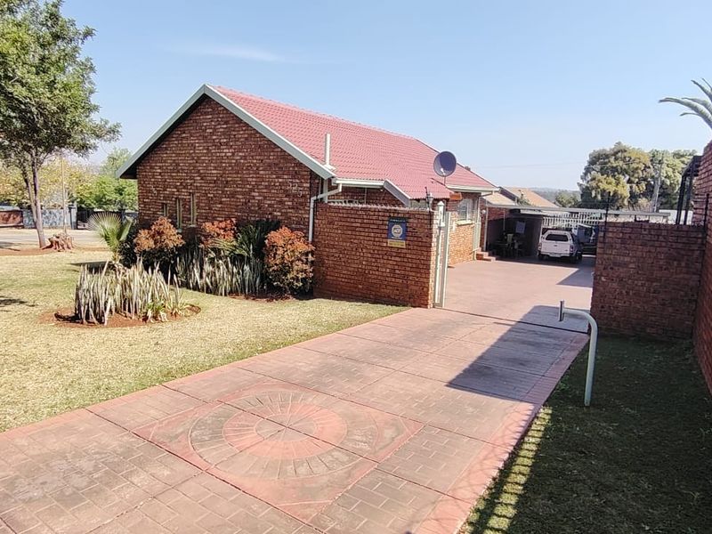 Front view of a brick house featuring a tiled roof, a paved driveway, and a secure boundary wall with perimeter fencing.